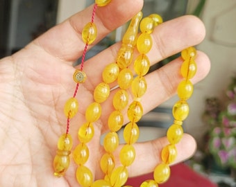 May include: A yellow amber prayer beads necklace with a gold accent. The beads are strung on a red cord.