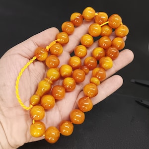 May include: A string of amber prayer beads with a tassel. The beads are a rich, golden yellow colour and have a smooth, polished finish.