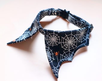 Op de afbeelding: Een Halloween-halsband voor huisdieren met een vleermuisvleugelontwerp. De zwarte halsband heeft een wit spinnenwebpatroon en oranje spinnen. Het heeft een metalen gesp en een D-ring. De lengte is ongeveer 30 cm.