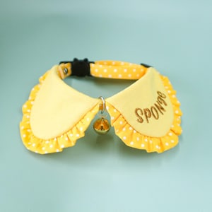 May include: Yellow polka dot cat collar with a ruffled edge and a gold bell. The collar has the word "Sponge" embroidered on it. The collar is secured with a black plastic buckle.