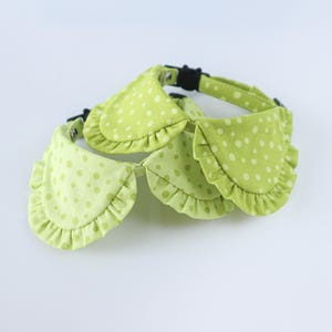 May include: A light green pet collar featuring a ruffled fabric design with a white polka dot pattern. The collar includes a black plastic side-release buckle and an adjustable strap, providing a secure fit for a pet's neck with a decorative ruffled edge.