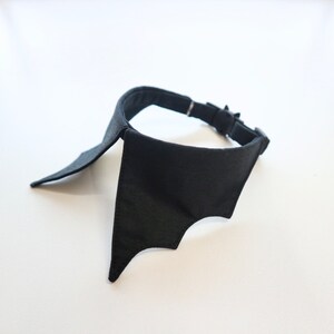 May include: A black bat-wing collar, likely for a pet. The collar is made of a solid black fabric and features a bat wing design on the front. It has a black adjustable strap with a silver-colored buckle.