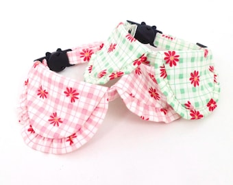 May include: Two dog collars with a ruffled trim and a gingham pattern with red flowers. The collars are pink and green.