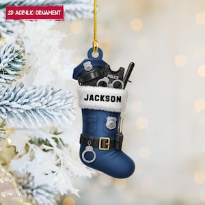 May include: A blue acrylic Christmas ornament shaped like a police officer's stocking, with the name "JACKSON" on the cuff. The stocking is filled with a police hat, handcuffs, and a baton. The ornament has a gold hanging string and the text "2D ACRYLIC ORNAMENT".