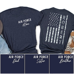 May include: Navy blue t-shirts with white text. One shirt says "AIR FORCE Mom" on the front. The back of the other shirt features an American flag design with the name "ROBERT" in white. Additional designs include "AIR FORCE Dad", "AIR FORCE Sister", and "AIR FORCE Brother".