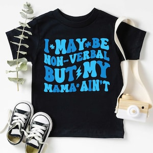Puede incluir: Camiseta negra de manga corta con texto azul que dice "I*MAY*BE NON-VERBAL BUT*MY MAMA*AIN'T".