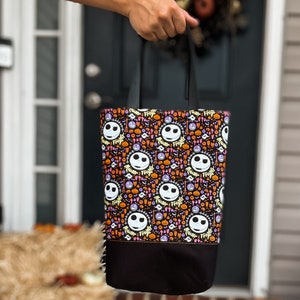 Puede incluir: Bolsa de tela negra y naranja con un patr&oacute;n repetido de la cara de Jack Skellington de Pesadilla Antes de Navidad. La bolsa tiene asas negras y un fondo negro.