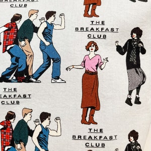 May include: A white fabric with a repeating pattern of characters from the movie The Breakfast Club. The characters are illustrated in a cartoon style and are wearing their iconic outfits from the film. The text "The Breakfast Club" is repeated throughout the fabric.