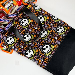 Puede incluir: Bolsa de tela negra y blanca con tem&aacute;tica de Halloween que presenta un patr&oacute;n repetido de la cara de Jack Skellington y las palabras "Master Fright". La bolsa tiene asas negras y est&aacute; hecha de una tela resistente.