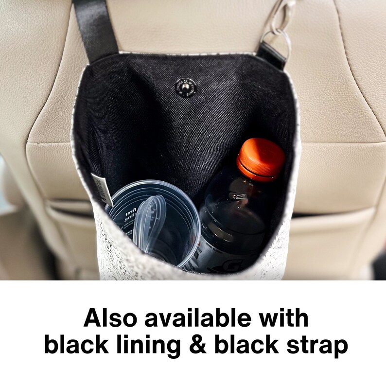 May include: A white and black patterned car seat organizer with a black strap. The organizer is hanging on the back of a car seat and contains a clear plastic cup and a dark bottle with an orange lid.