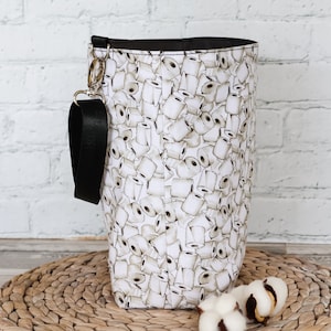 Peut inclure: Sac fourre-tout en toile blanche avec une sangle noire et un imprim&eacute; de rouleaux de papier toilette. Le sac est pos&eacute; sur un tapis de paille tress&eacute;.