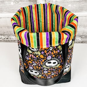 Puede incluir: Una bolsa de tela negra y naranja con tem&aacute;tica de Halloween con un forro de tela a rayas. La bolsa presenta un patr&oacute;n repetido de personajes de Jack Skellington y las palabras "Master of Fright".
