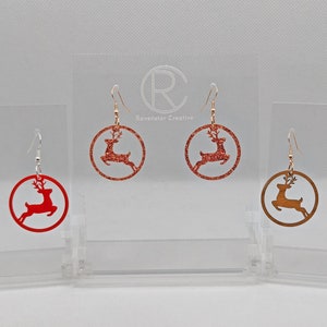May include: Three pairs of dangle earrings featuring a red, rose gold, and gold reindeer silhouette on a circular background. The earrings are displayed on a white background.