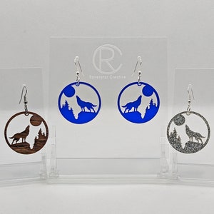 May include: Three pairs of wolf howling at the moon earrings. The earrings are made of wood, blue acrylic, and silver glitter. The earrings are all round and have a silver hook.