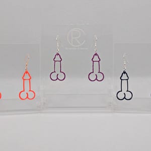 May include: Three pairs of dangle earrings with a unique design. The earrings are made of acrylic and come in three colors: orange, purple, and black.
