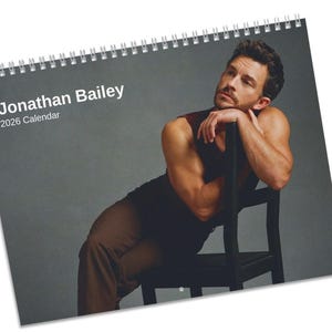 Könnte beinhalten: Ein Spiral-Kalender für 2026 mit einem Foto von Jonathan Bailey. Auf dem Cover steht "Jonathan Bailey 2026 Calendar". Das Bild zeigt einen Mann in einem dunklen ärmellosen Oberteil und braunen Hosen, der auf einem schwarzen Stuhl lehnt.