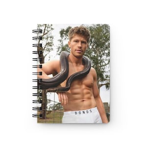 May include: Spiral-bound notebook featuring a photograph of a person with a snake around their neck. The person is wearing white underwear with the word "BONDS" printed on the waistband. The background includes a fence and trees.
