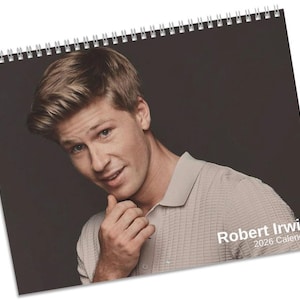 Op de afbeelding: Spiraalgebonden kalender met een portret van Robert Irwin. De afbeelding toont een man in een lichtgekleurd overhemd met kraag tegen een donkere achtergrond. De tekst "Robert Irwin 2026 Calendar" staat rechtsonder.