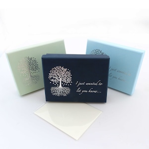 May include: Three rectangular gift boxes in pastel colors: light green, navy blue, and light blue. Each box features a silver tree design and the text "I just wanted to let you know...". A small, off-white card rests in front.