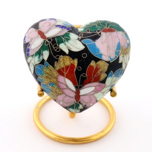 May include: A black heart-shaped trinket box with a gold stand. The box is decorated with colourful enamel butterflies and floral designs.