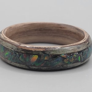 May include: A wooden ring with a band of iridescent opal inlay. The ring is a light brown color and the opal inlay is a mix of green, blue, and orange.