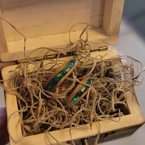 May include: Two wooden rings with green opal inlay, nestled in a wooden box lined with brown straw.