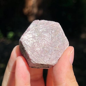 May include: A pink and white gemstone with a hexagonal shape and a rough, textured surface.