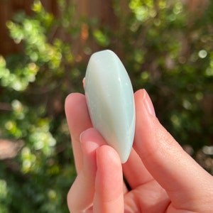 May include: A smooth, light green, oval-shaped polished stone with a white swirl pattern.