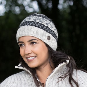 May include: A woman wearing a white and gray striped knit beanie with a black button on the side. The beanie is made of wool and has a soft, comfortable feel.