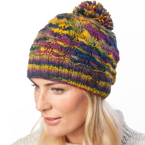 May include: A colourful knitted beanie with a pom pom on top. The beanie is made of a soft, warm yarn and features a variety of colours, including purple, yellow, green, and blue.