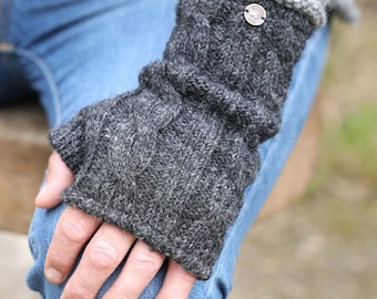 May include: Gray knitted fingerless gloves with a cable knit design. The gloves have a button detail on the cuff and are made of a soft, textured yarn. The gloves are designed to keep hands warm while leaving fingers free.