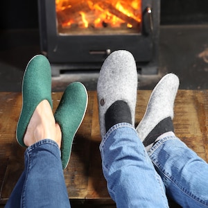 May include: Two pairs of felt slippers, one green and one gray, worn by two people sitting in front of a fireplace.