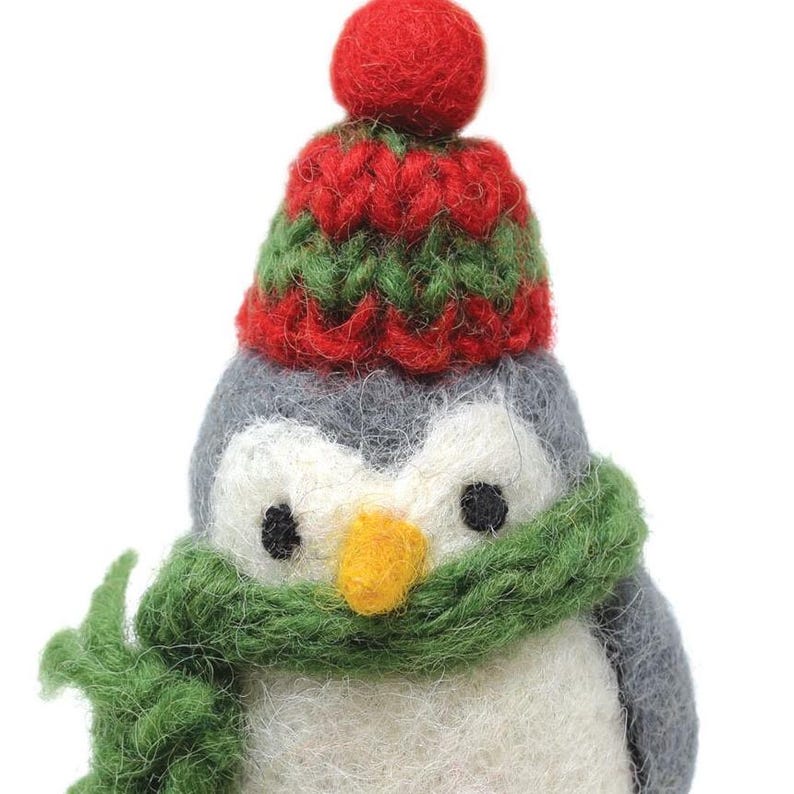 May include: A gray and white penguin wearing a red and green knit hat with a pom-pom and a green scarf.