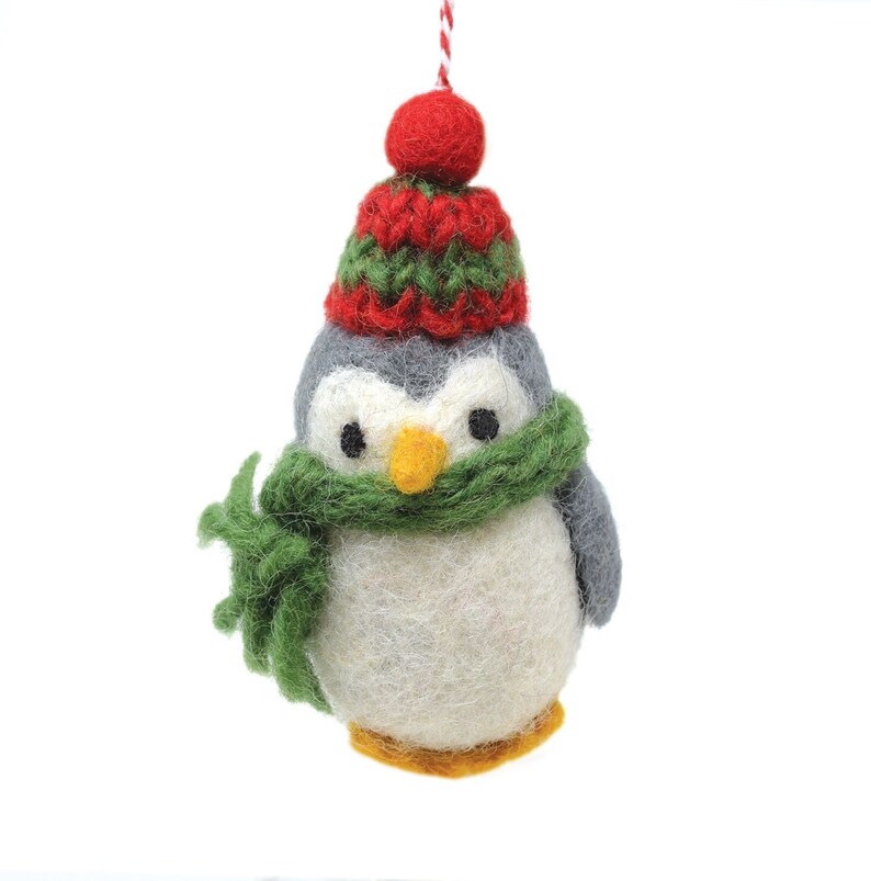 May include: A felt penguin ornament wearing a green scarf and a red and green knit hat.