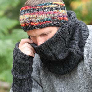 Peut inclure: Une personne porte un pull gris, un cache-cou gris foncé et des mitaines assorties. Un bandeau tricoté coloré avec des accents rouges, jaunes, bleus et verts est également porté.