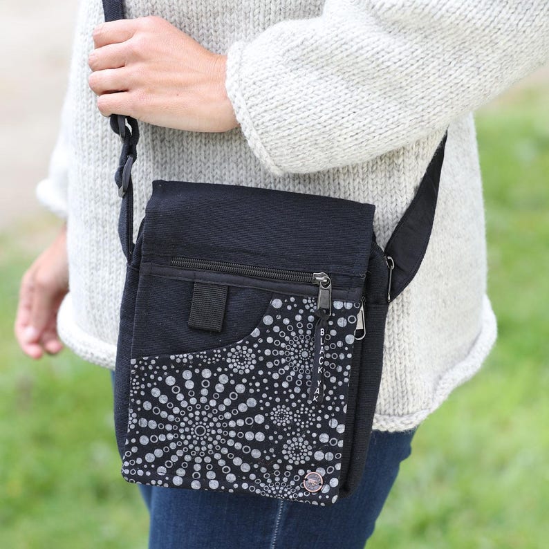 May include: A black canvas crossbody bag with a zippered pocket and a white and black patterned pocket. The bag has a long adjustable strap.