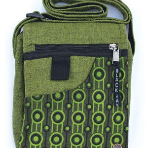 May include: A green canvas crossbody bag with a black zipper and a black and green geometric pattern on the front flap. The bag has a black strap and a small black pocket on the front. The bag has a black "BLACK YAK" tag hanging from the zipper.