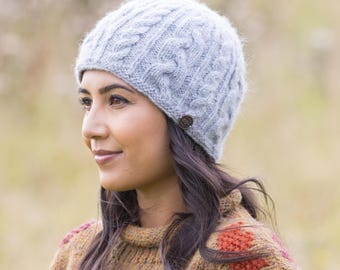 Puede incluir: Un gorro de punto trenzado gris claro con un pequeño botón marrón. El gorro presenta un diseño clásico de punto trenzado y está hecho de un hilo suave y texturizado. Un accesorio elegante para el clima frío.