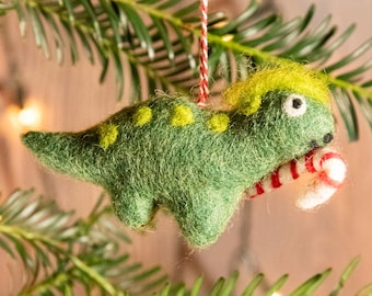 May include: Green felt dinosaur Christmas ornament holding a candy cane. The dinosaur has yellow spots and a yellow tuft of hair on its head.
