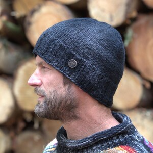 May include: A dark grey knitted beanie hat with a small, round button detail on the side. The hat is made of a textured yarn and has a ribbed brim. A winter accessory.