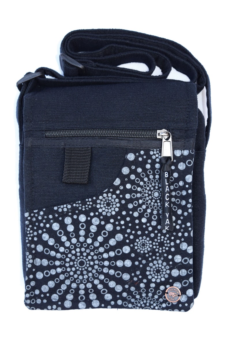 May include: Black canvas crossbody bag with a zipper closure and a small pocket on the front. The pocket has a white and black circular pattern with the text "Black Yak" on the side.