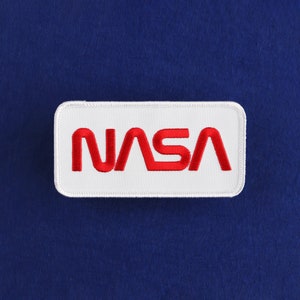 Może przedstawiać: Biała naszywka haftowana z czerwonym logo NASA.