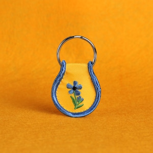 May include: A yellow key chain with a blue flower embroidered on it.
