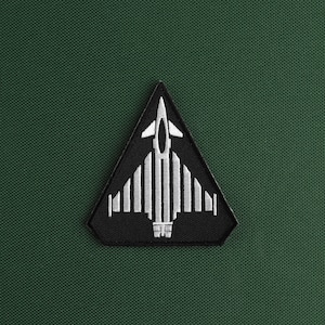 Peut inclure: Un écusson triangulaire noir avec une image brodée blanche d'un avion de chasse.