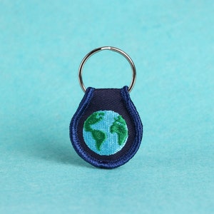 May include: A blue and green key chain with a silver ring and an embroidered image of the Earth.