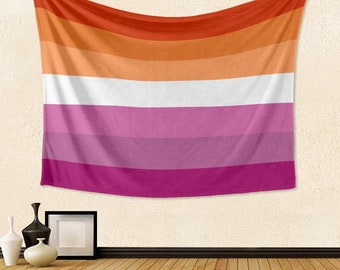 Op de afbeelding: Een lesbische vlag hangt aan een witte muur. De vlag heeft zes horizontale strepen: oranje, lichtoranje, wit, roze, lichtpaars en paars.
