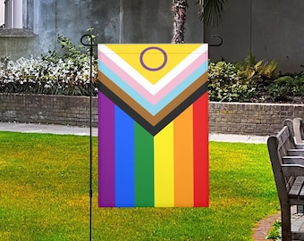 Puede incluir: Una bandera de jardín rectangular con un diseño vibrante. La sección superior es amarilla con un círculo morado, seguida de una serie de chevrones de colores. La mitad inferior muestra rayas verticales de arcoíris. La bandera está en un soporte de metal negro.