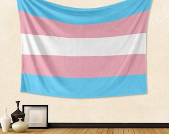 Puede incluir: Una bandera del orgullo transgénero colgada en una pared. La bandera tiene cinco franjas horizontales: azul claro, rosa, blanco, rosa y azul claro.