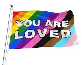 Puede incluir: Una bandera del orgullo arcoíris con las palabras "You Are Loved" en letras blancas. La bandera tiene rayas de rojo, naranja, amarillo, verde, azul, añil, violeta, rosa, negro, marrón, azul claro y rosa claro.
