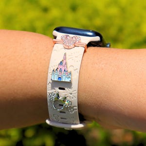 May include: A white Apple Watch band with a pink and white castle charm, a pink and white Mickey Mouse charm, and a silver Mickey Mouse charm with rhinestones.
